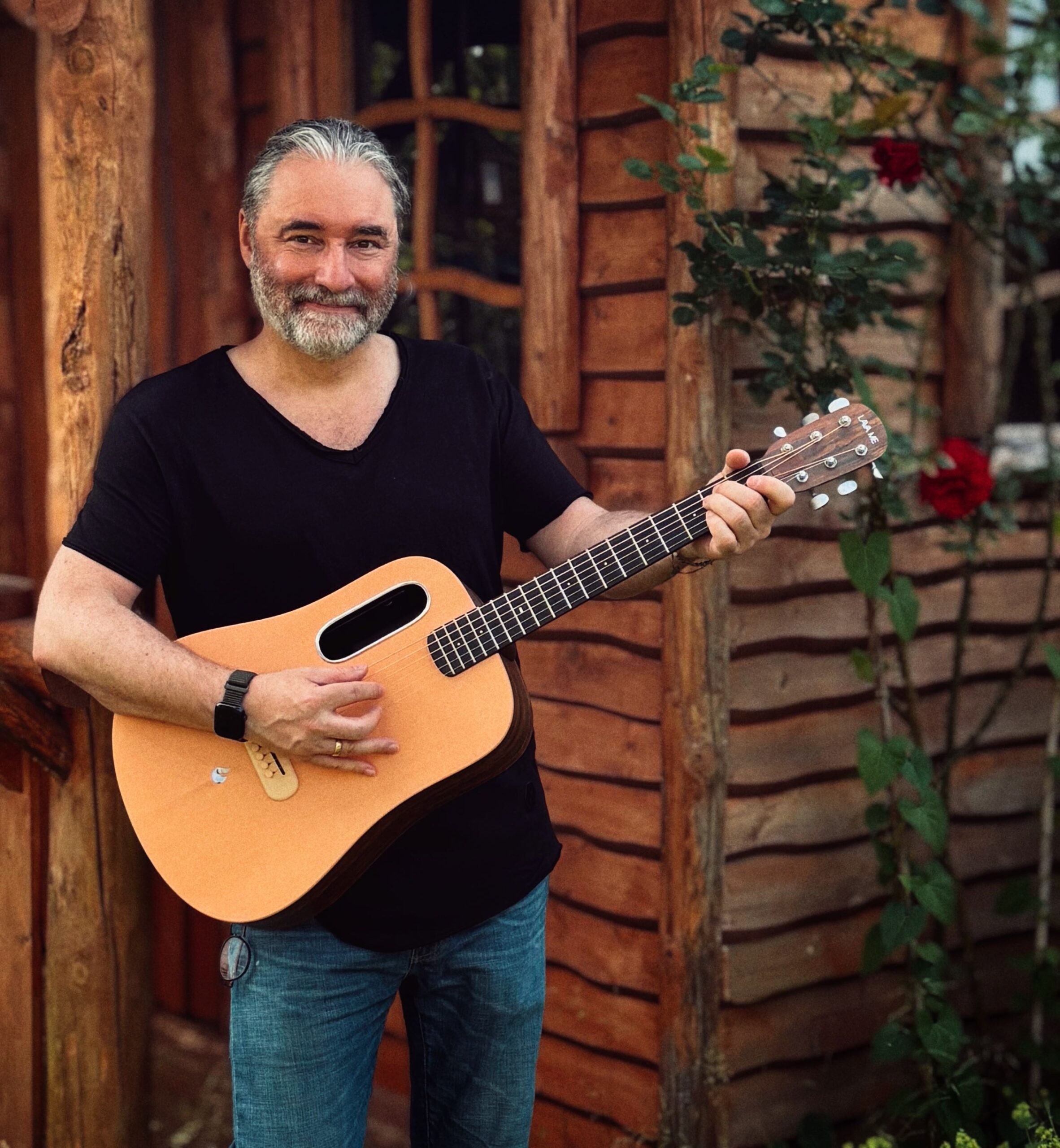 Tommy mit der LAVA ME 4 Spruce Smart Guitar vor einer Holzhütte. Die Decke der Gitarre besteht aus Fichtenholz. Die Öffnung ist oberhalb der Seiten.